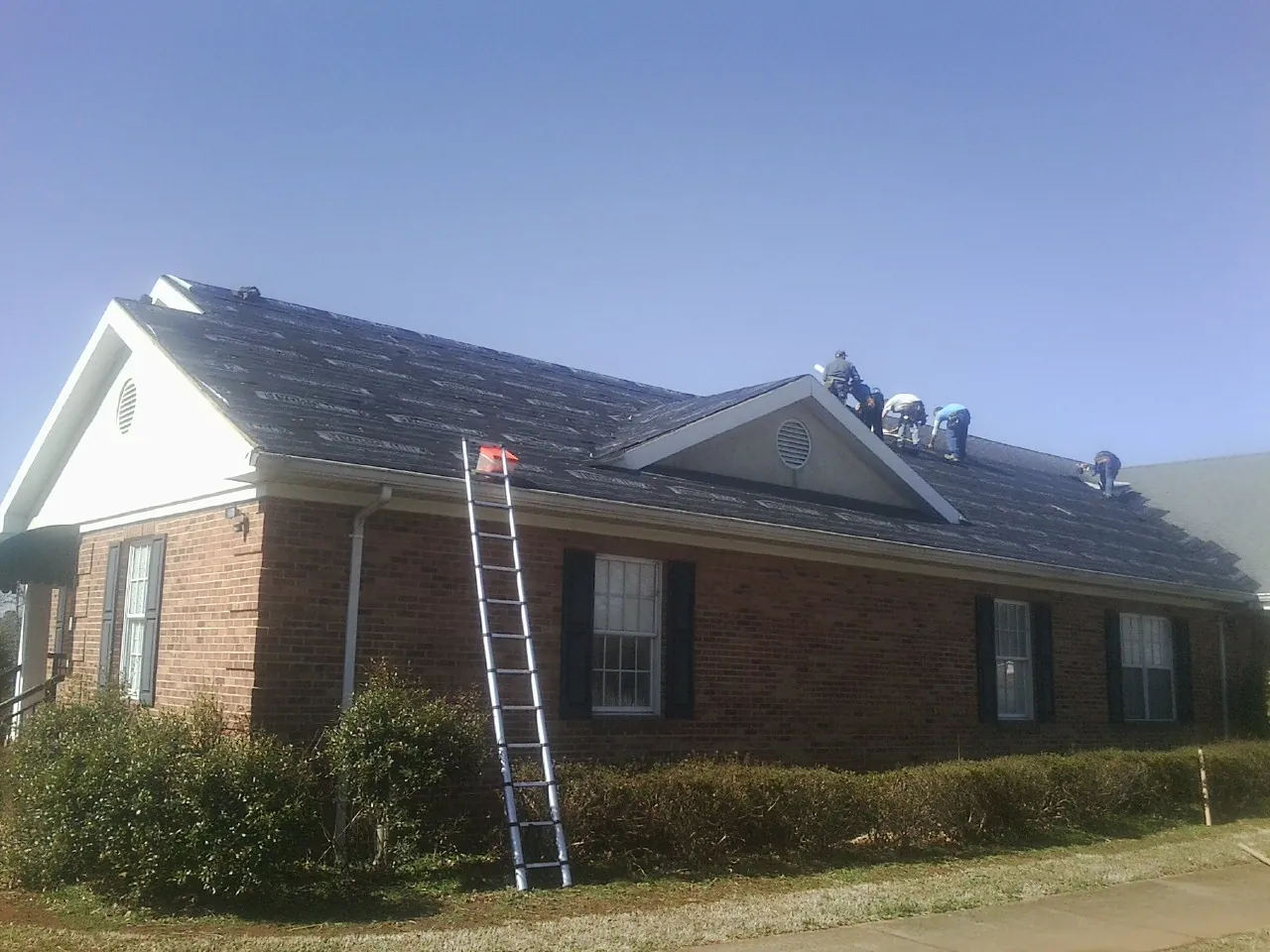 Crew tearing shingles off a brick ranch roof with a ladder set — Metal Roof Repair work by our crew in Lakeville