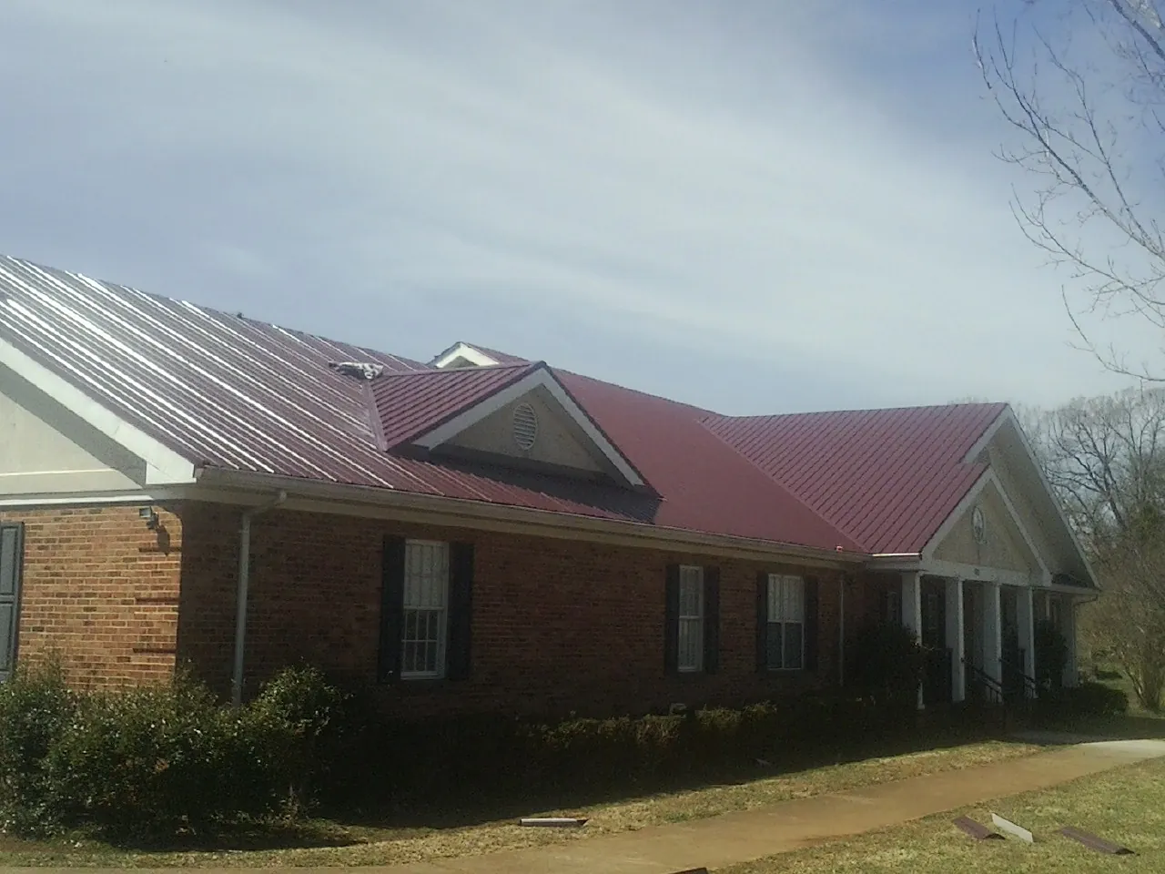 Red metal roof with gabled entries on a long brick building, from a Hail Damage Roof Repair job in Lakeville
