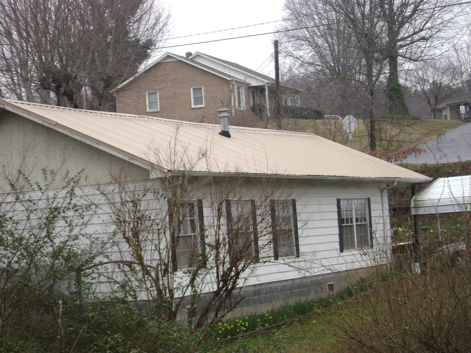 Tan metal roof on a white sided house set into a hillside — Commercial Roofing by Roofing Brothers in Lakeville